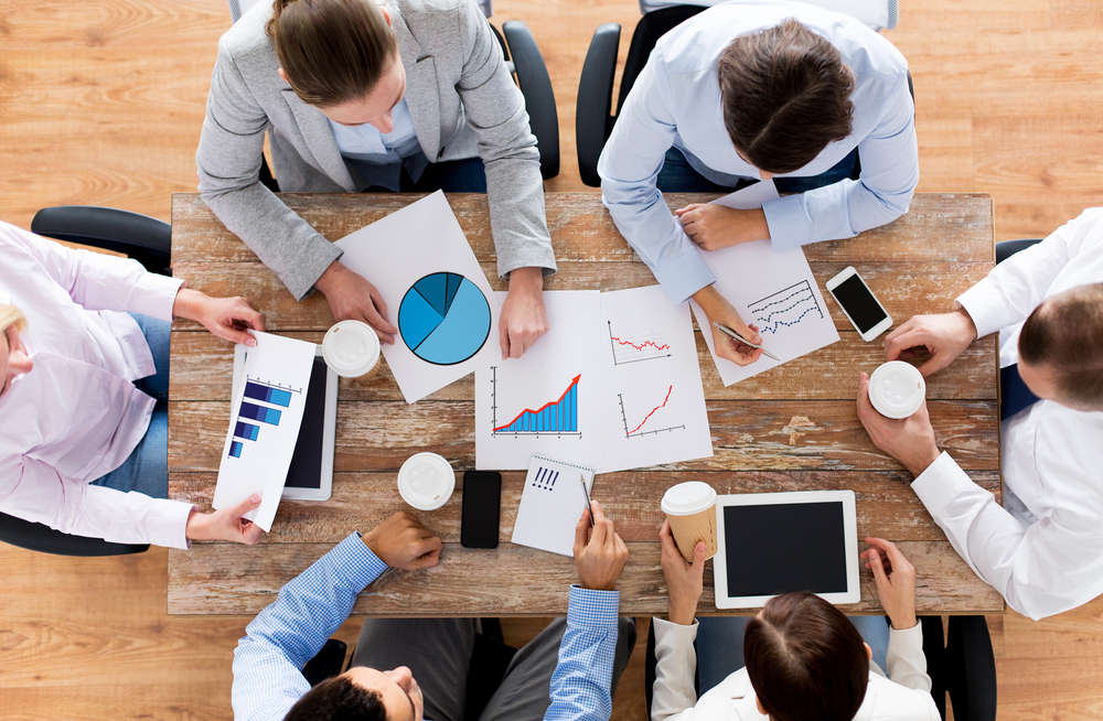 Overhead view of a meeting where people are analyzing charts and graphs